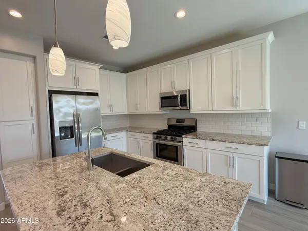 a kitchen with stainless steel appliances granite countertop a sink a stove a refrigerator cabinets and chairs