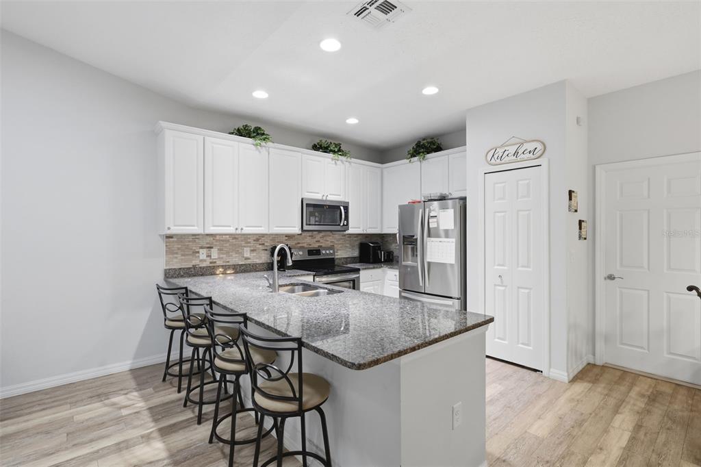205 Merlot Street DeLand, FL 32724 - Photo 6 of 34 a kitchen with kitchen island granite countertop a refrigerator a stove a sink and white cabinets with wooden floor