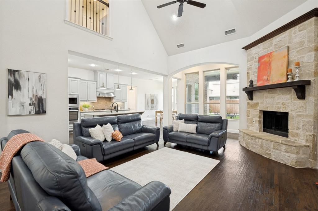 14215 Raspberry Lane Frisco, TX 75035 - Photo 5 of 30 Vaulted ceiling living area featuring a stone fireplace with wood mantel, dark wood-finish flooring, and arched windows