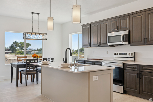 5777 West 4100 South Hooper, UT 84315 - Photo 8 of 41 Kitchen with stainless steel appliances, light wood-type flooring, decorative light fixtures, light stone counters, and a kitchen island with sink