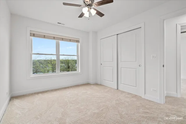 an empty room with chandelier fan and windows