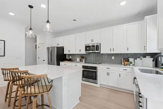 a kitchen with stainless steel appliances kitchen island granite countertop a sink a stove a refrigerator and white cabinets with wooden floor