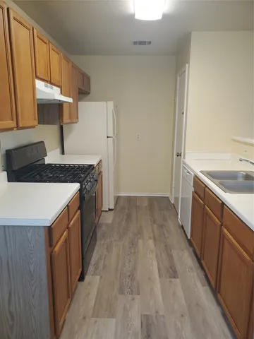 an empty room with wooden floor kitchen view and windows