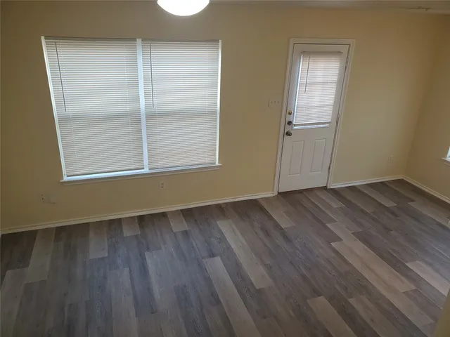 an empty room with wooden floor kitchen view and windows