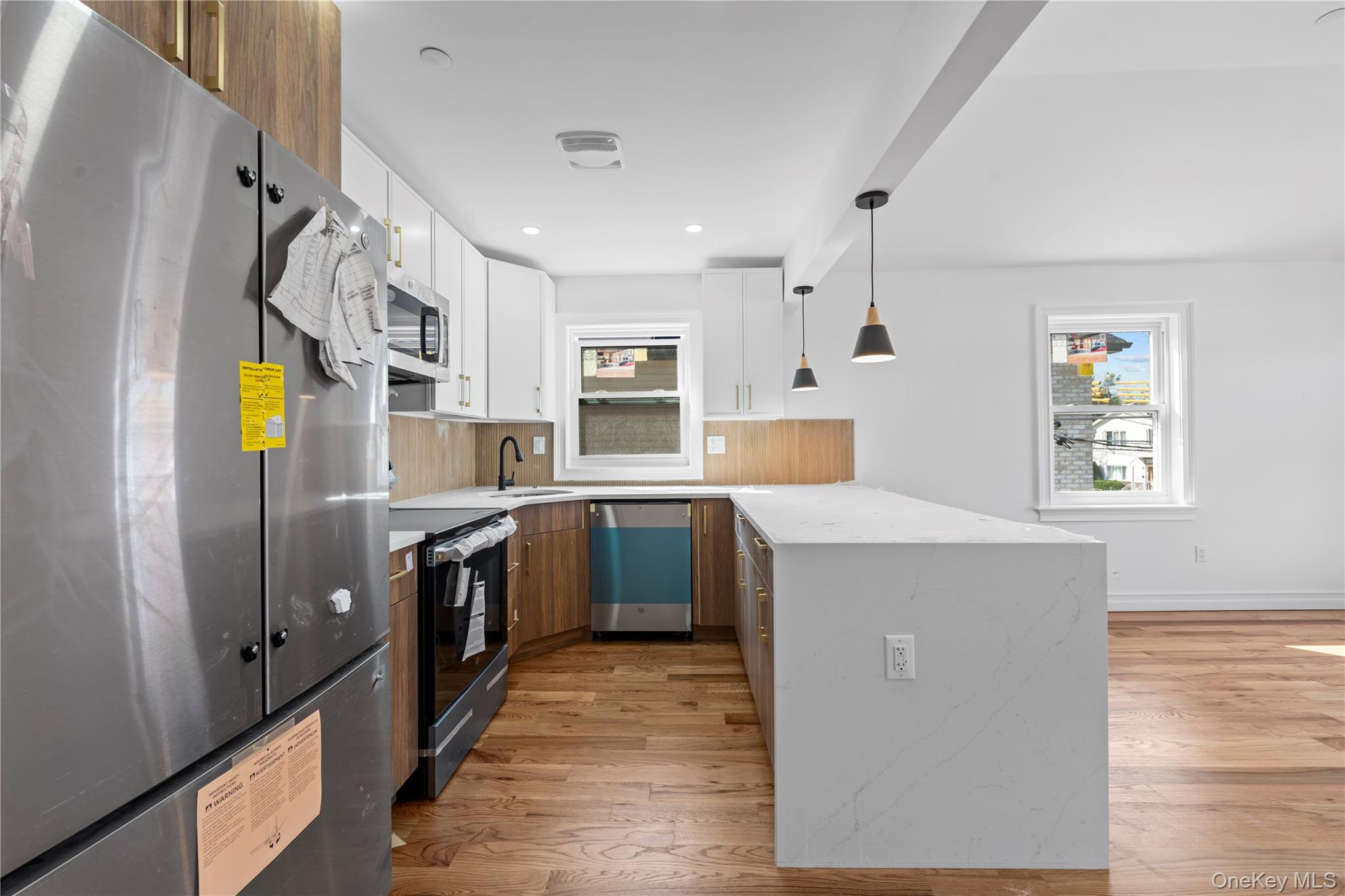 258-14 147th Road Queens, NY 11422 - Photo 14 of 22 Kitchen featuring stainless steel appliances, white cabinetry, brown cabinetry, a peninsula, and backsplash