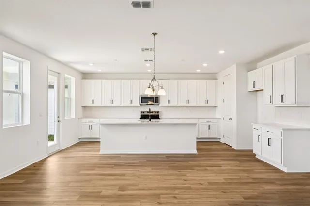 a view of kitchen with stainless steel appliances granite countertop a sink a stove a refrigerator and white cabinets
