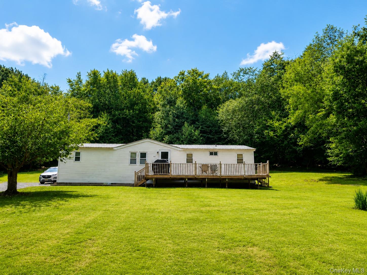 182-184 Mutton Hill Road Neversink, NY 12765 - Photo 1 of 36 Expansive green lawn surrounds a single-story residence with a full-length wood deck and a backdrop of mature trees