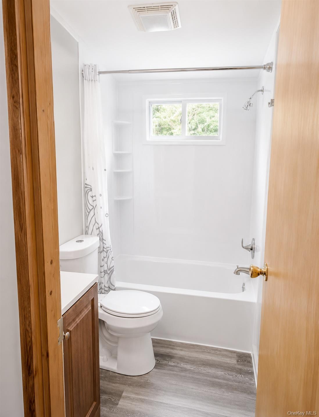 182-184 Mutton Hill Road Neversink, NY 12765 - Photo 16 of 36 Full bathroom featuring a white tub and shower combination with chrome fixtures, a window above the tub, a ventilation fan, a toilet, and wood-finish flooring