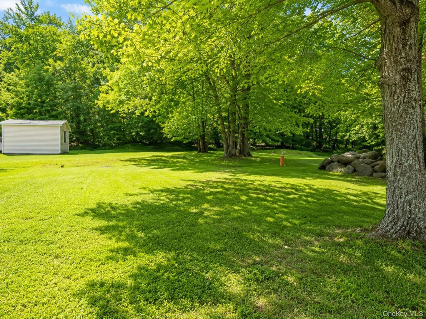 182-184 Mutton Hill Road Neversink, NY 12765 - Photo 21 of 36 Expansive green lawn surrounded by mature trees, featuring a white storage shed with a window and a natural rock formation