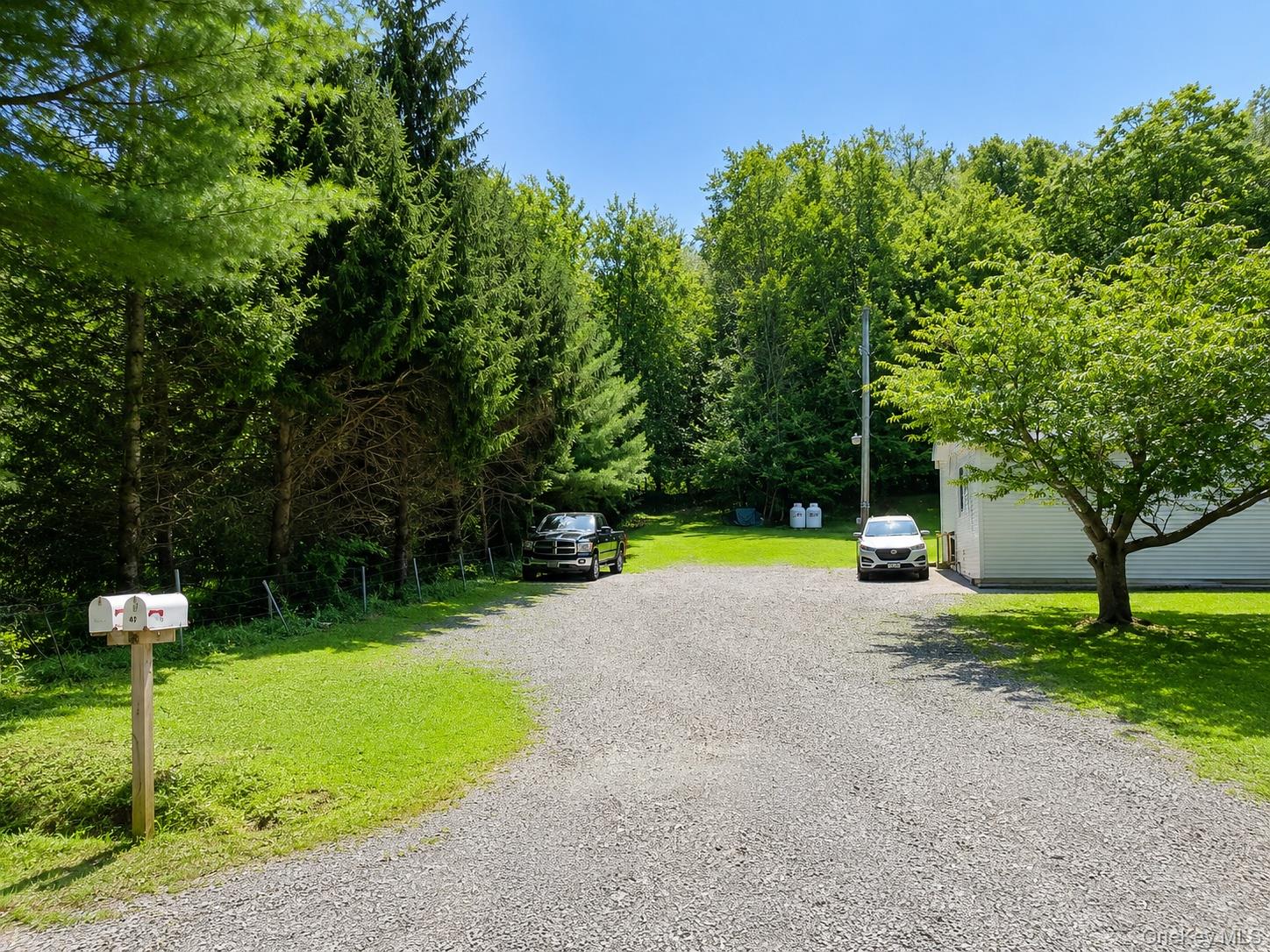 182-184 Mutton Hill Road Neversink, NY 12765 - Photo 36 of 36 Gravel driveway surrounded by mature trees, a manicured lawn, and a white-sided structure