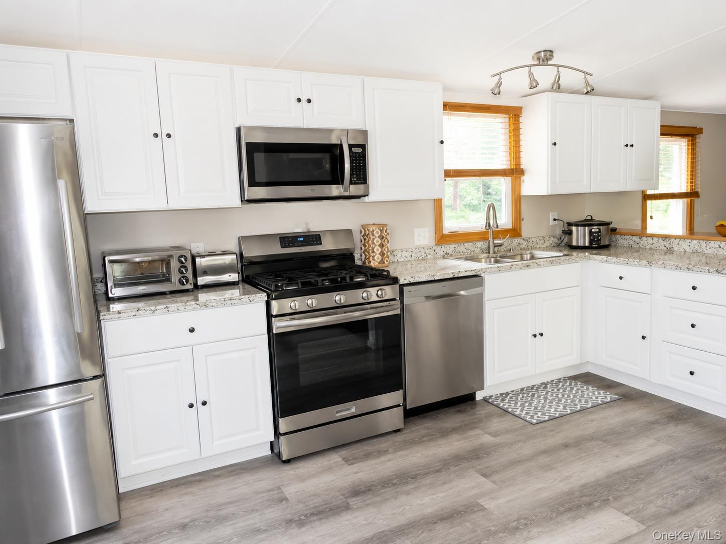 182-184 Mutton Hill Road Neversink, NY 12765 - Photo 5 of 36 Kitchen featuring white cabinetry, stainless steel appliances, speckled countertops, a double basin sink with a gooseneck faucet, and wood-finish flooring