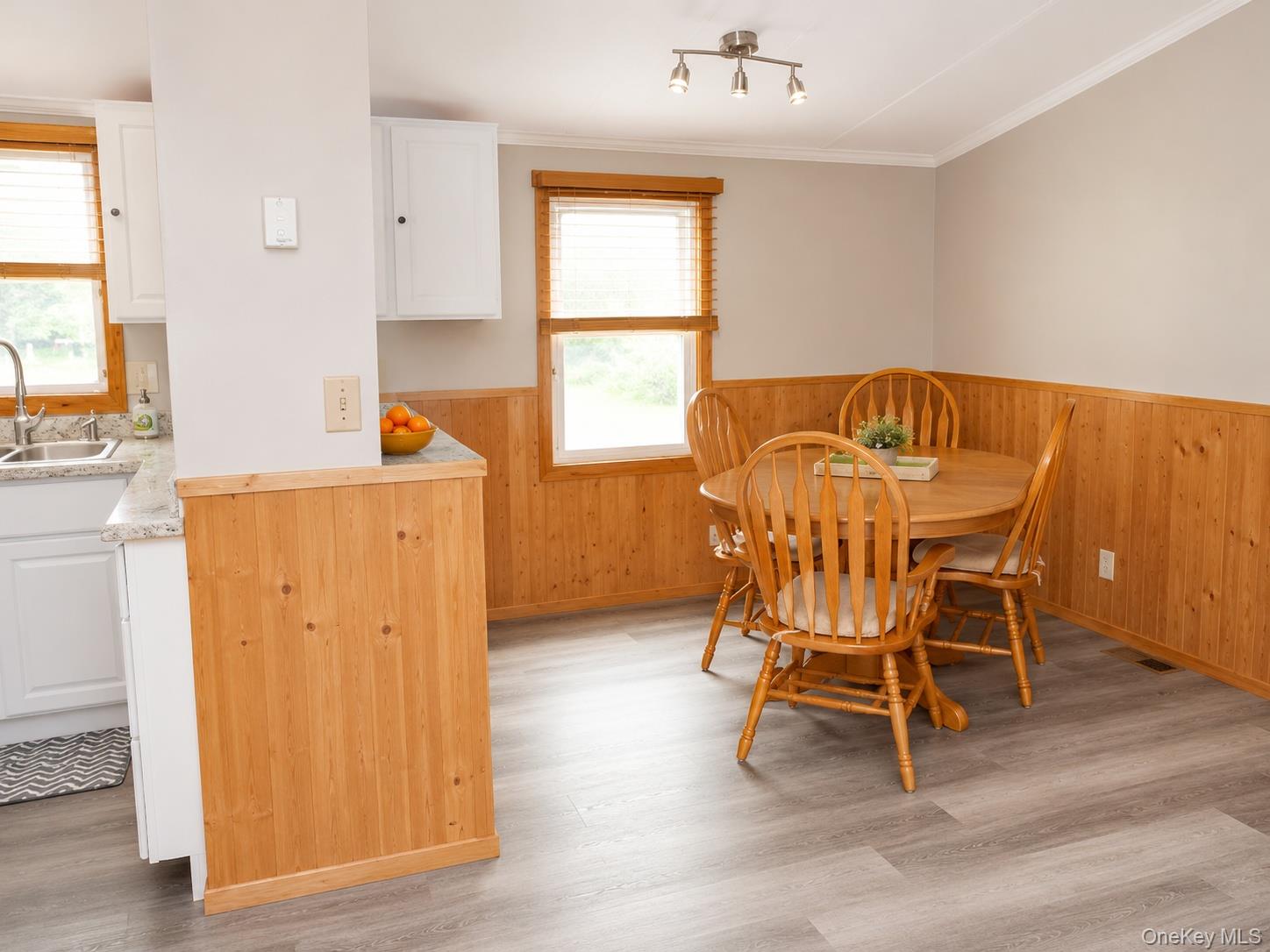 182-184 Mutton Hill Road Neversink, NY 12765 - Photo 8 of 36 Kitchen and dining area featuring wood-finish flooring, half-wall wood paneling, white upper and lower cabinetry, and a stainless steel sink with a gooseneck faucet