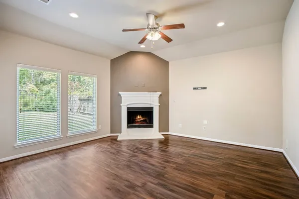 a view of an empty room with wooden floor fireplace and a window