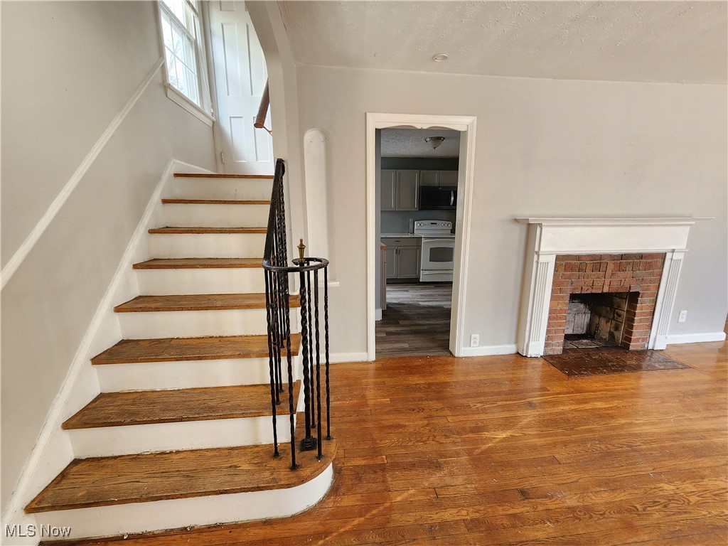1160 Brentwood Road Cleveland, OH 44121 - Photo 4 of 26 Staircase with a brick fireplace, hardwood floors, and a textured ceiling