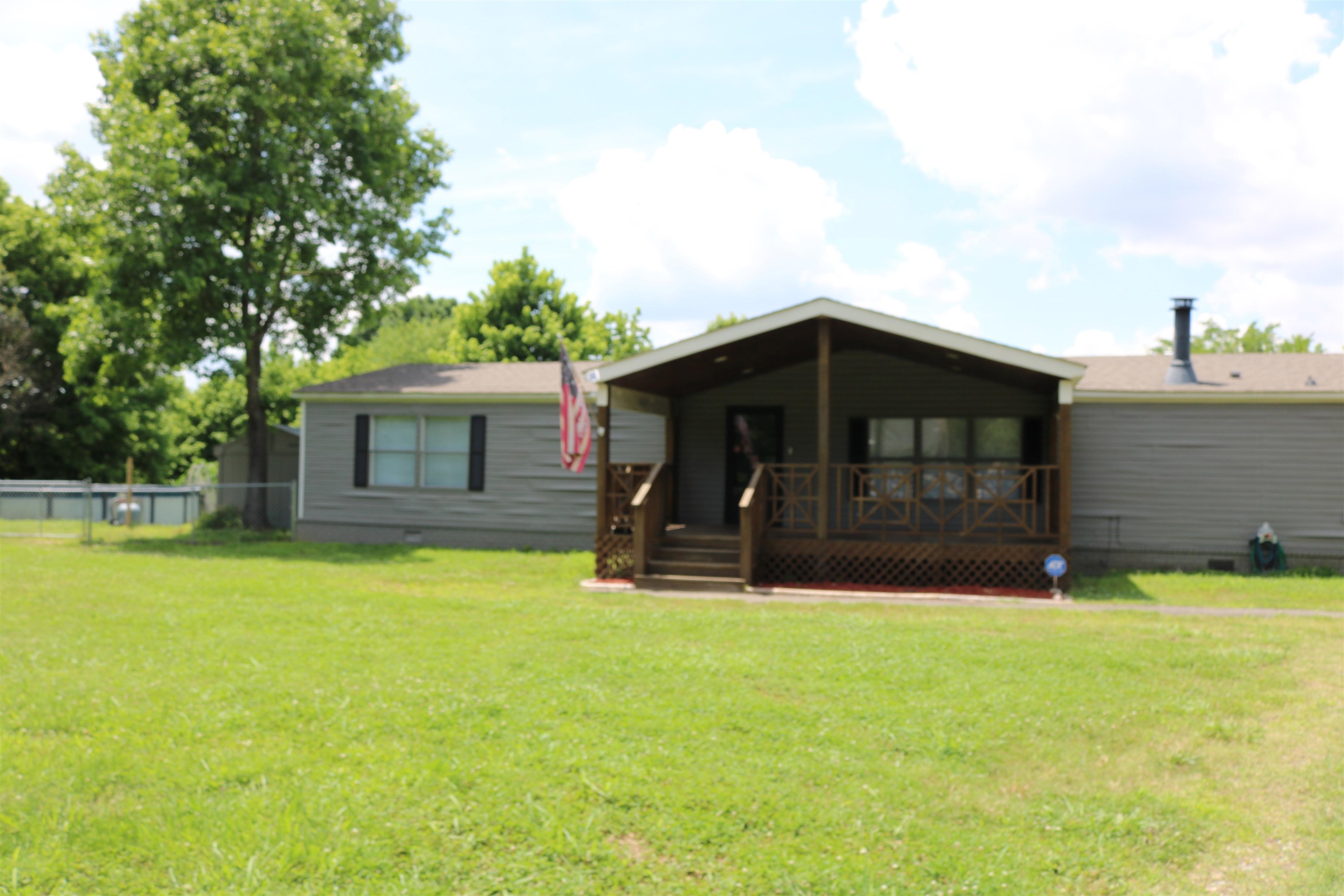 Exterior featuring a covered porch with wood railing, gray siding and a mature tree