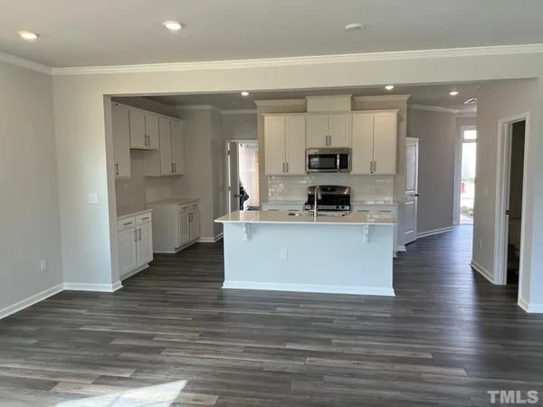 a large kitchen with stainless steel appliances granite countertop a stove a sink a refrigerator and white cabinets with wooden floor