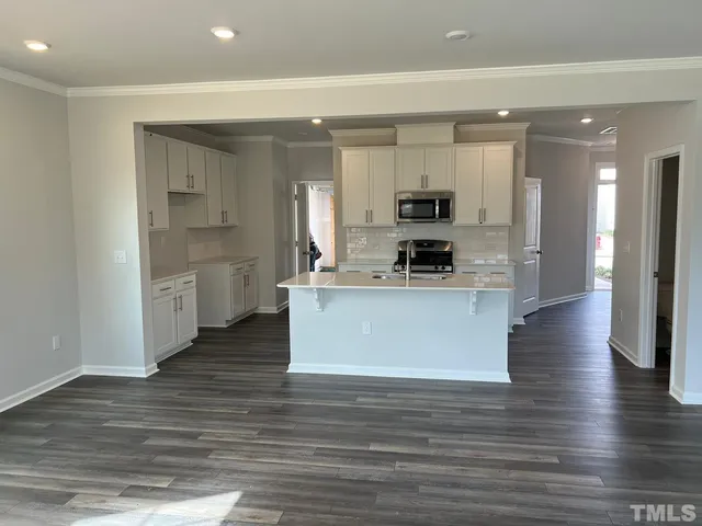 a large kitchen with stainless steel appliances granite countertop a stove a sink a refrigerator and white cabinets with wooden floor