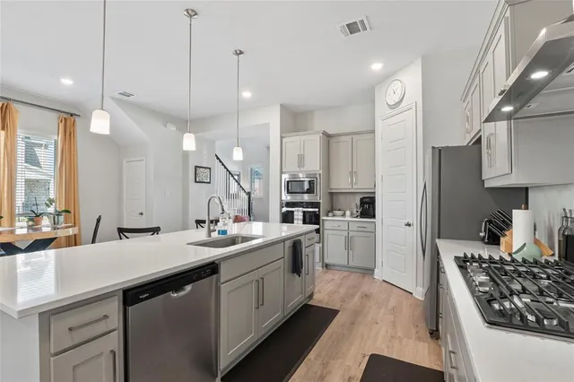 a kitchen with stainless steel appliances kitchen island granite countertop a refrigerator a stove a sink dishwasher and white cabinets with wooden floor