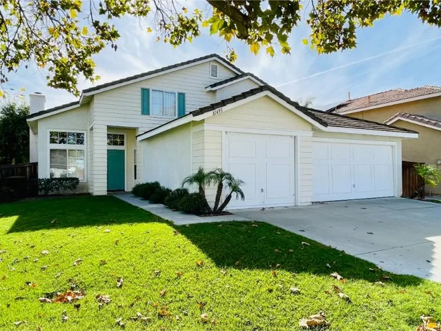 a view of a white house with a yard plants and large tree