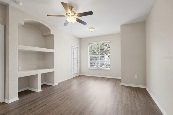 an empty room with wooden floor chandelier fan and windows