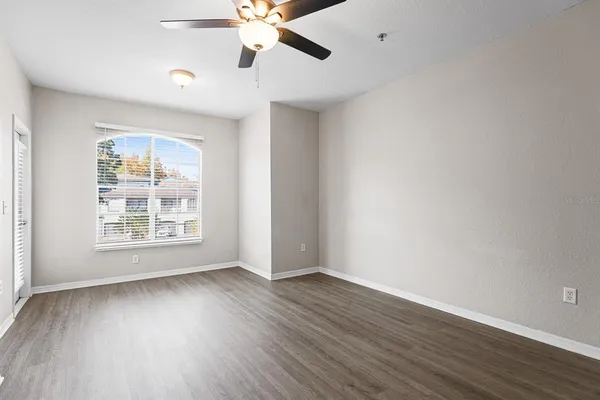 an empty room with wooden floor chandelier fan and windows