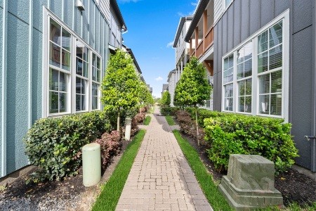 614 Delmar Street Houston, TX 77023 - Photo 2 of 24 This photo showcases a charming walkway between two modern townhouses, featuring lush greenery, hedges, and neatly trimmed trees. The path is paved with bricks, offering a welcoming and well-maintained outdoor space.