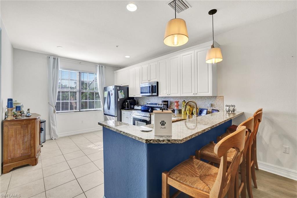 9115 Capistrano Street South, Unit 8207 Naples, FL 34113 - Photo 9 of 29 a kitchen with stainless steel appliances granite countertop a sink a stove a dining table and chairs