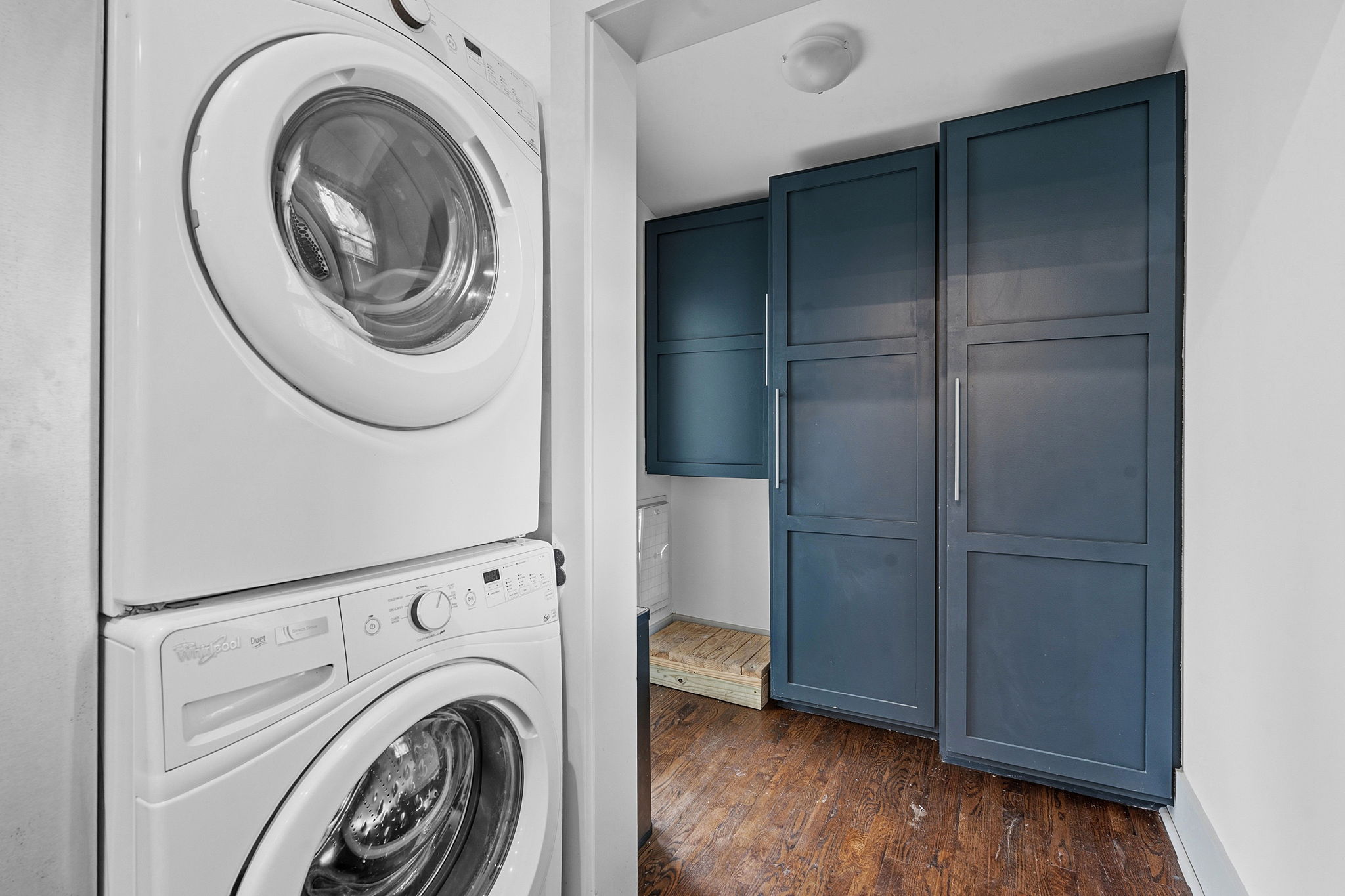 1122 Gunter Street Austin, TX 78702 - Photo 14 of 23 Dedicated laundry area featuring a stacked appliance unit, dark wood-finish flooring, and built-in teal cabinetry with silver hardware