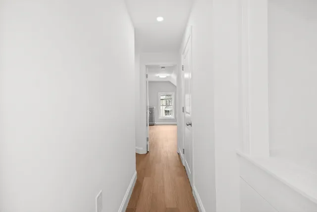 a view of a hallway with wooden floor and a bathroom