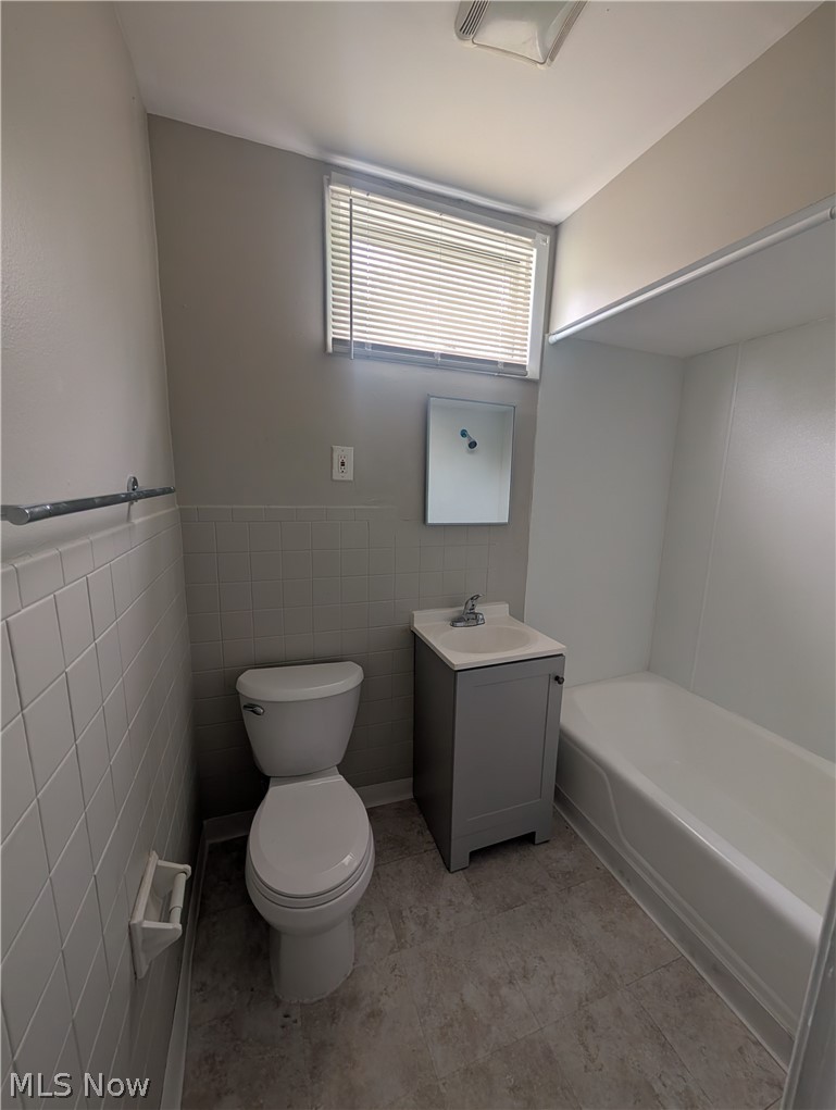 7515 Ottawa Road Cleveland, OH 44105 - Photo 20 of 21 Bathroom featuring a white bathtub, gray vanity with integrated sink, toilet, and a window with blinds