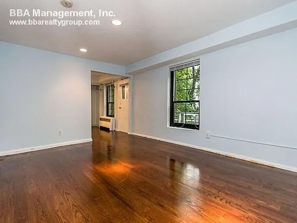 a view of an empty room with wooden floor and a window