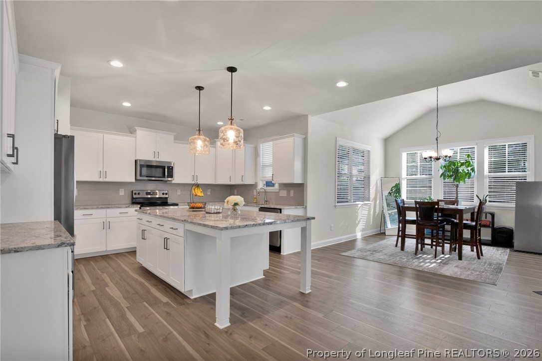224 Timber Skip Drive Spring Lake, NC 28390 - Photo 10 of 30 a kitchen with stainless steel appliances kitchen island granite countertop a stove top oven a sink a dining table and chairs with wooden floor