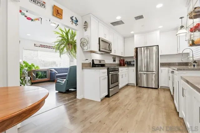 a kitchen with stainless steel appliances granite countertop a refrigerator a stove a sink dishwasher and white cabinets with wooden floor