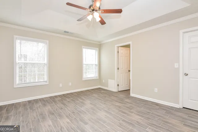 an empty room with wooden floor chandelier fan and windows