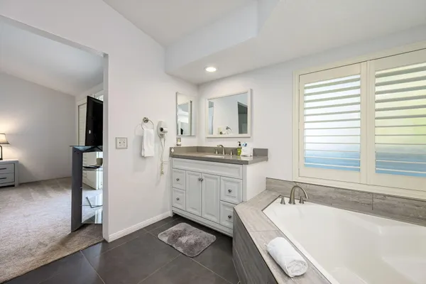 a bathroom with a granite countertop sink mirror bathtub and next to a window