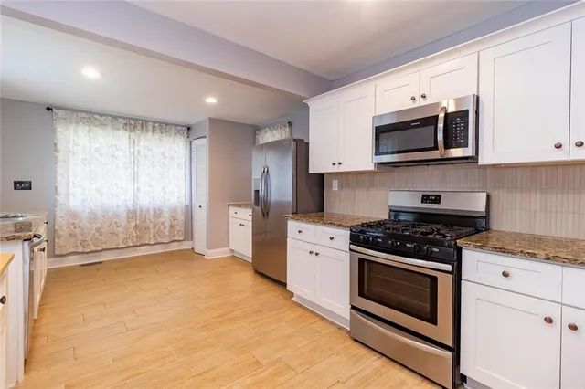 a kitchen with stainless steel appliances granite countertop a stove a microwave and white cabinets