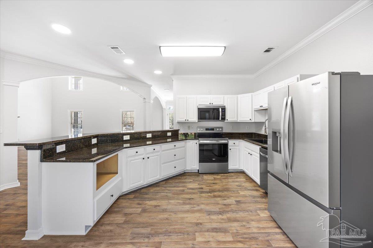 2099 Garcon Point Road Milton, FL 32583 - Photo 25 of 65 a kitchen with stainless steel appliances granite countertop a stove top oven a refrigerator and white cabinets with wooden floor