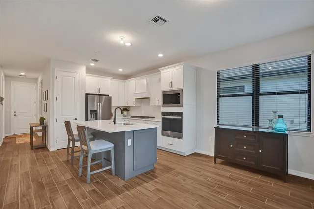 a kitchen with stainless steel appliances a kitchen island a stove a sink a refrigerator and white cabinets with wooden floor