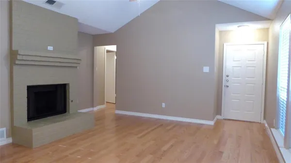 a view of an empty room with wooden floor and a fireplace