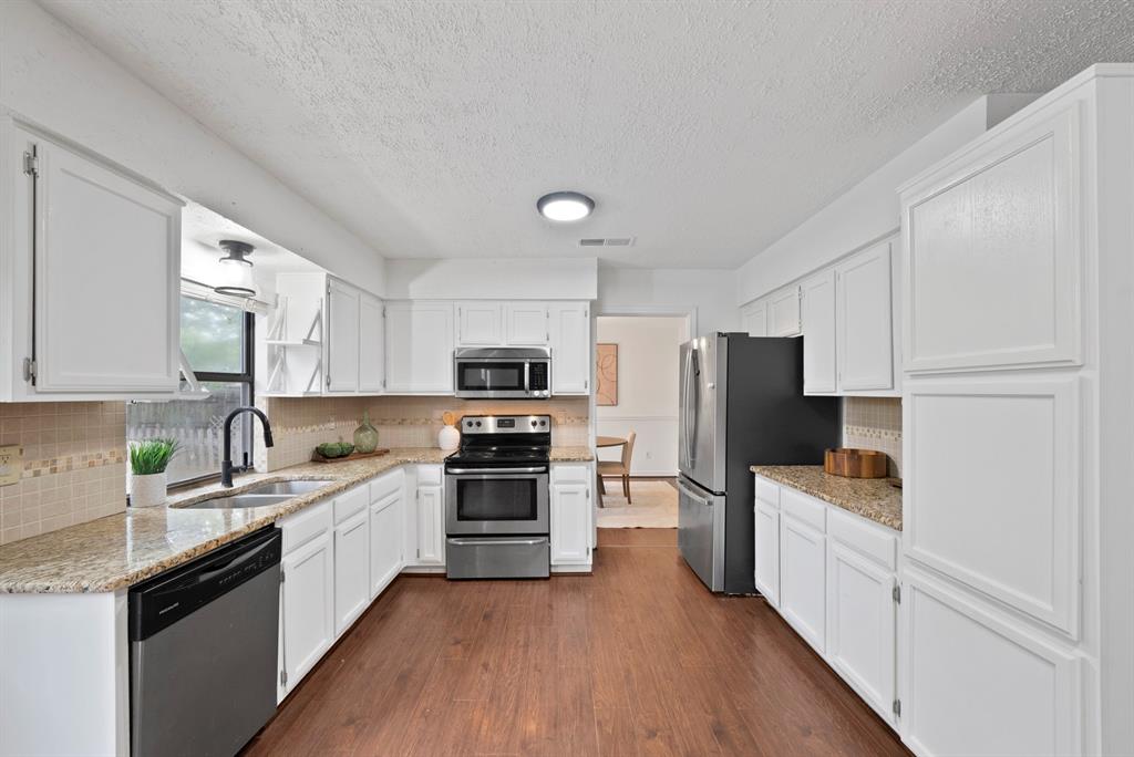 413 Wild Oak Lane Euless, TX 76039 - Photo 9 of 29 a kitchen with stainless steel appliances a sink dishwasher a refrigerator oven a sink dishwasher and white cabinets with wooden floor