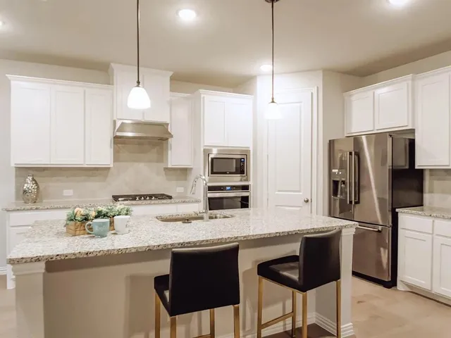 a kitchen with stainless steel appliances granite countertop a sink a stove a refrigerator and island with wooden cabinets