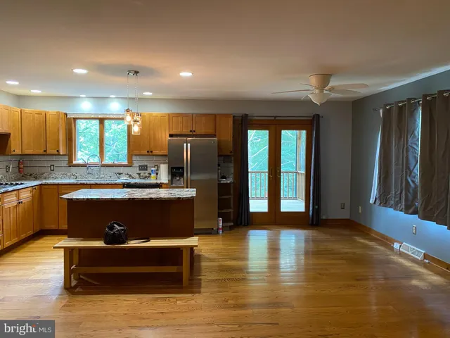 a kitchen with stainless steel appliances granite countertop a refrigerator a sink dishwasher and a large mirror with wooden floor