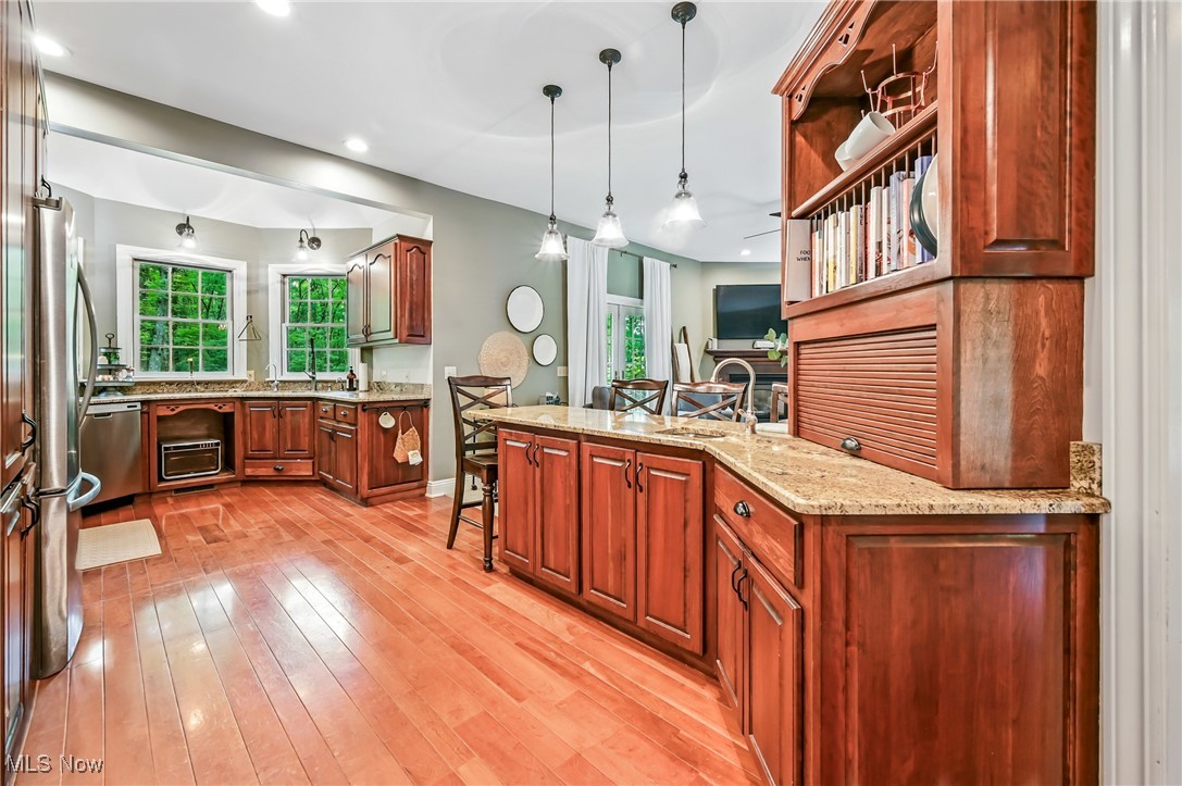 1681 State Road Northwest Warren, OH 44481 - Photo 27 of 50 Kitchen with wood flooring, pendant lighting, appliances with stainless steel finishes, light stone counters, and a kitchen bar