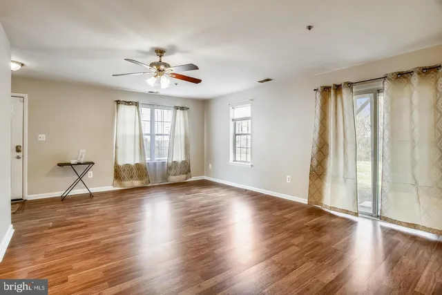 an empty room with wooden floor fan and windows