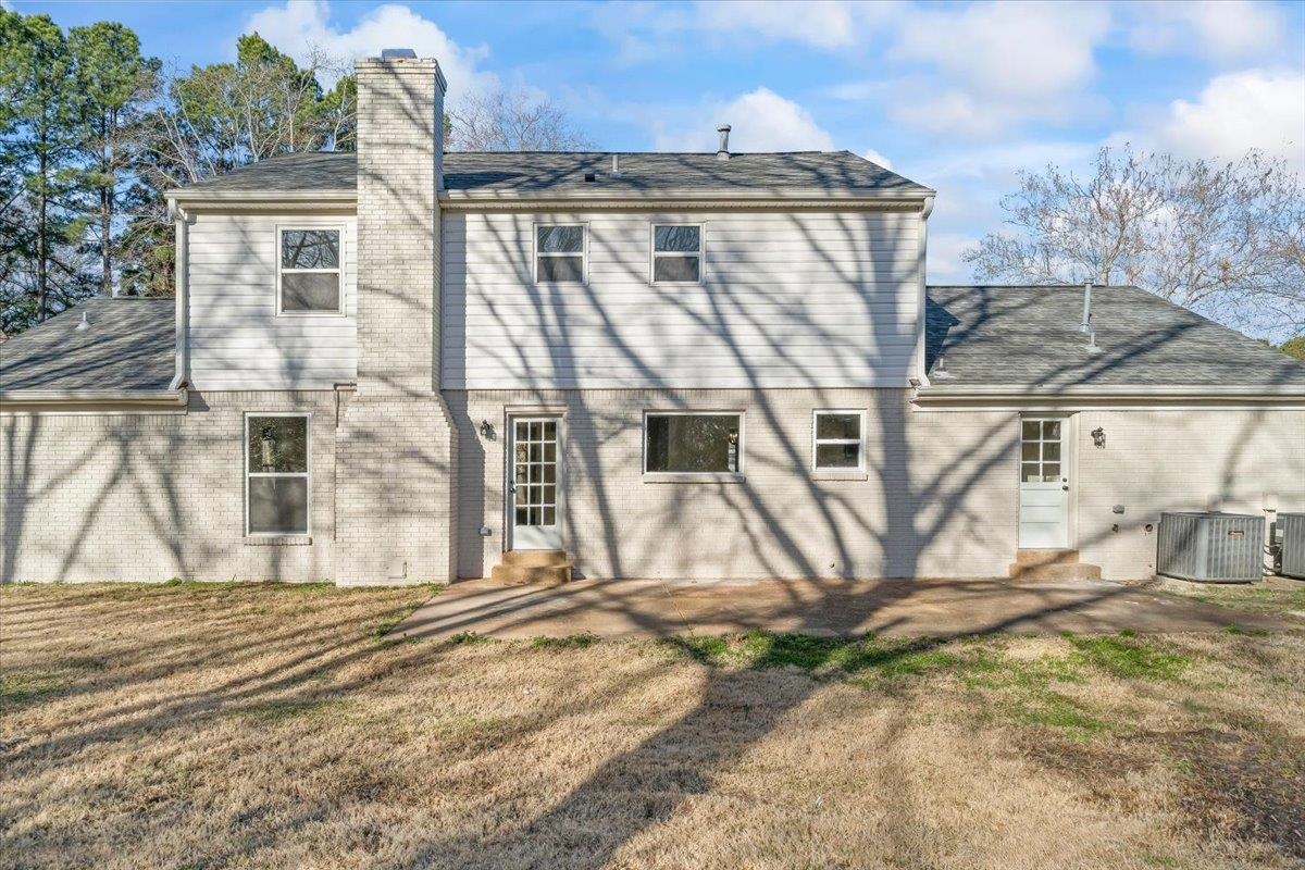 1676 Miller Farms Road Germantown, TN 38138 - Photo 29 of 37 Rear exterior featuring painted brick and horizontal siding, a prominent brick chimney, multiple windows, and two entry doors