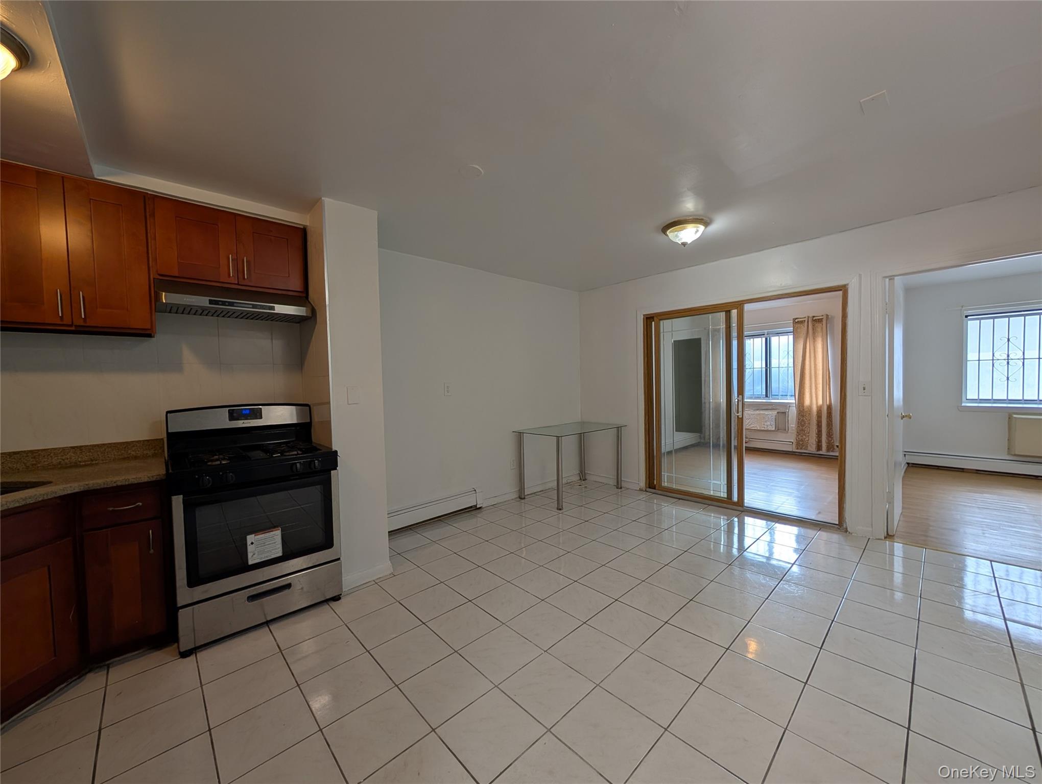 Kitchen featuring stainless steel gas range oven, exhaust hood, a baseboard heating unit, a baseboard radiator, and light tile patterned flooring
