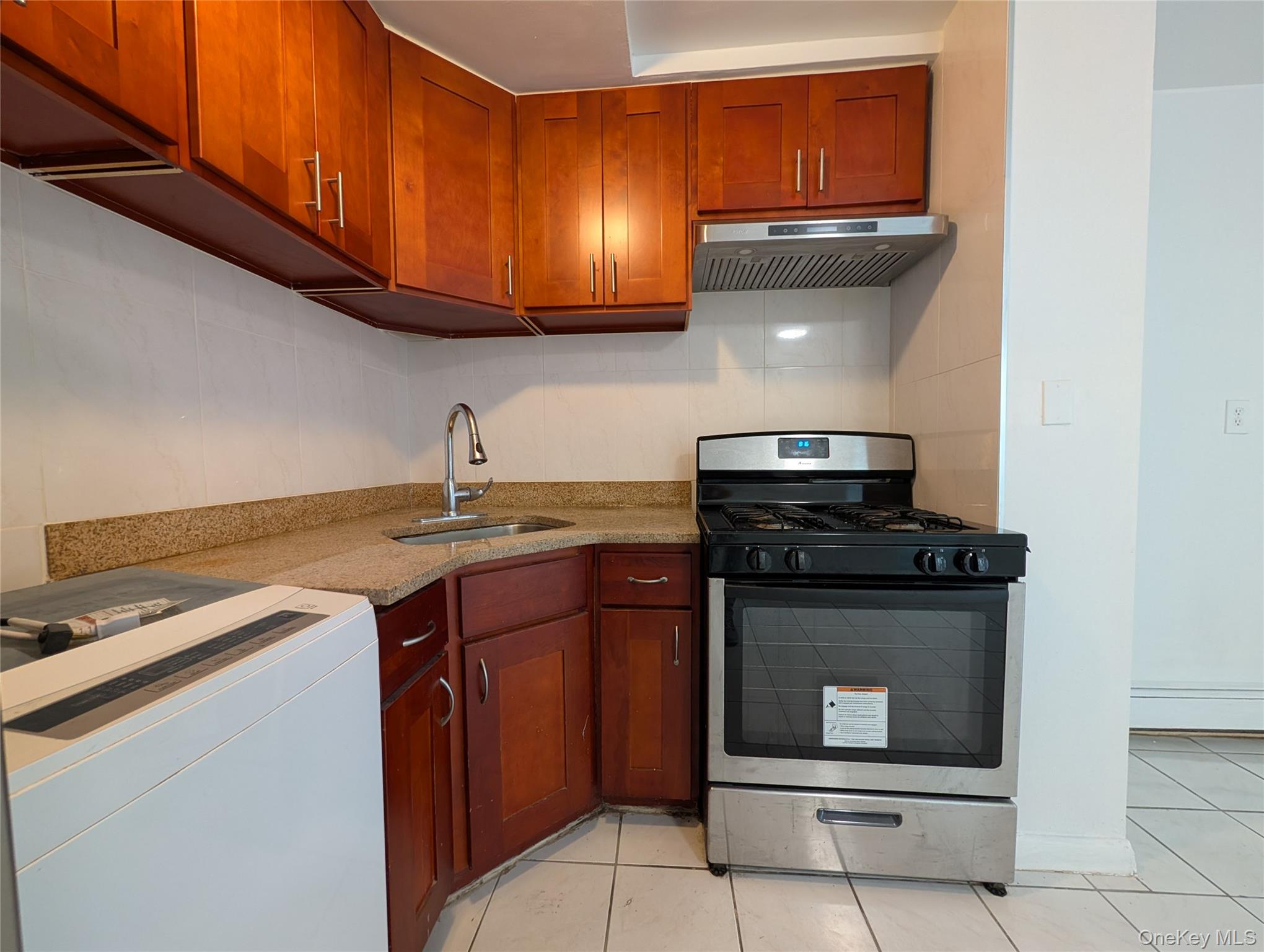 43-04 158th Street, Unit L4 Queens, NY 11358 - Photo 3 of 21 Kitchen with stainless steel gas stove, extractor fan, washer / clothes dryer, light tile patterned floors, and light stone counters