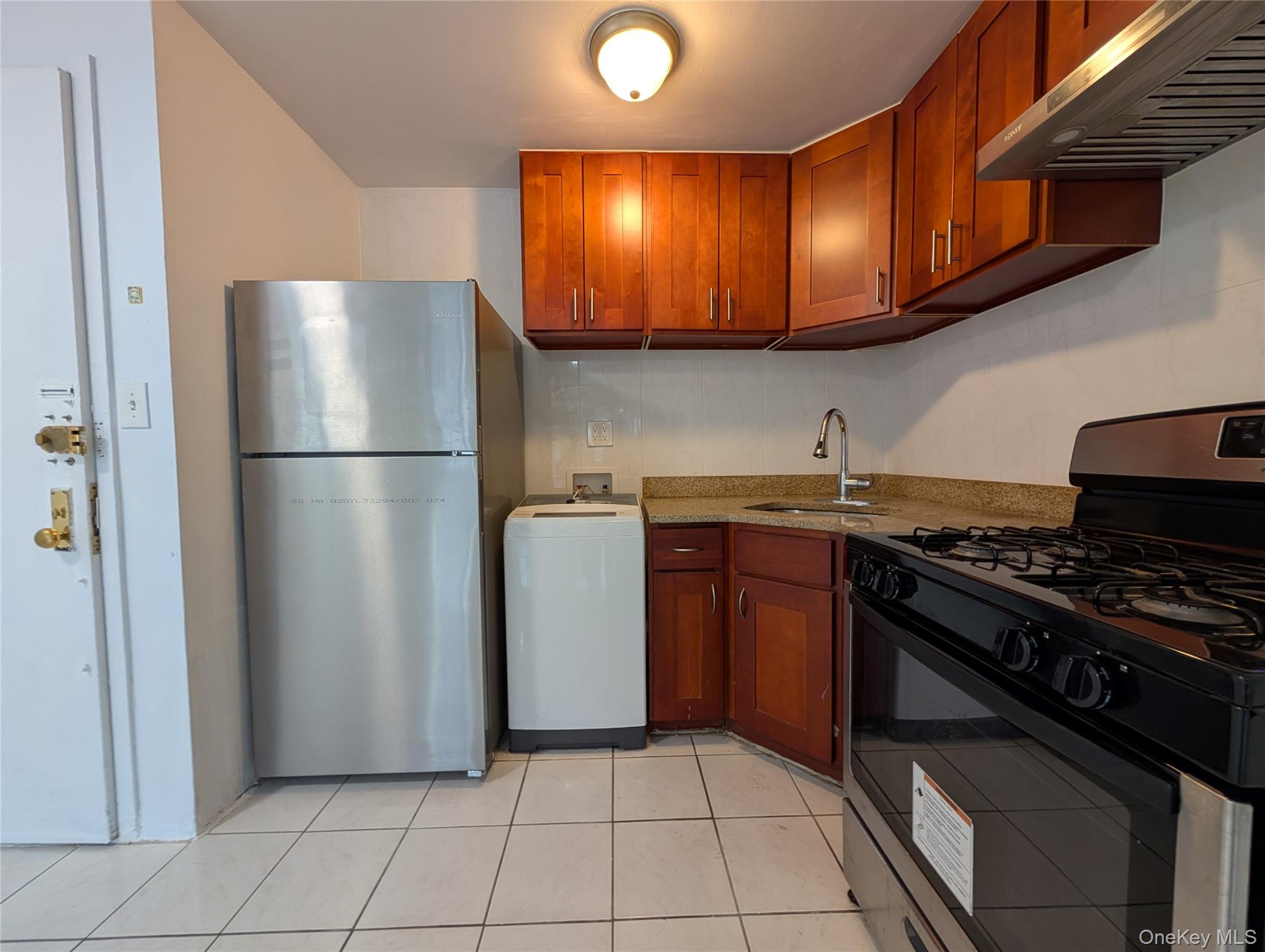 43-04 158th Street, Unit L4 Queens, NY 11358 - Photo 5 of 21 Kitchen with range with gas cooktop, freestanding refrigerator, under cabinet range hood, brown cabinets, and light tile patterned floors