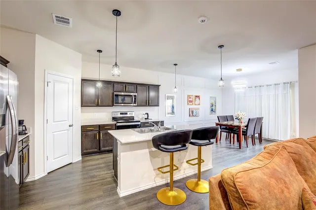 a kitchen with stainless steel appliances kitchen island granite countertop a stove a refrigerator a kitchen island a dining table and chairs with wooden floor