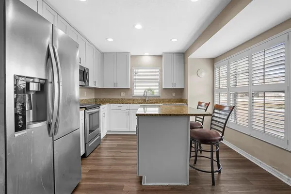 a kitchen with stainless steel appliances granite countertop a refrigerator a sink dishwasher a stove and white cabinets with wooden floor
